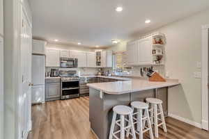 Kitchen featuring a peninsula, light wood-style flooring, gray cabinetry, a breakfast bar area, and appliances with stainless steel finishes