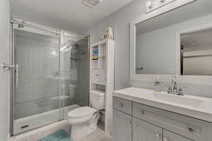 Bathroom featuring toilet, a textured ceiling, visible vents, and a stall shower