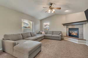 Carpeted living area featuring a tile fireplace, baseboards, a ceiling fan, and vaulted ceiling