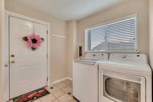 Clothes washing area with light tile patterned floors, independent washer and dryer, laundry area, and baseboards