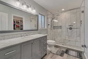 Full bath with toilet, a stall shower, wood finished floors, and vanity