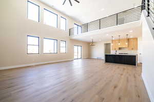 Unfurnished living room with light wood-style flooring, a towering ceiling, visible vents, a sink, and baseboards
