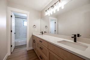 Full bathroom featuring double vanity, baseboards, a sink, and wood finished floors