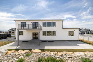 Rear view of house with a patio, a balcony, fence, and stucco siding