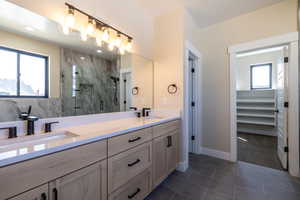 Full bathroom with double vanity, a marble finish shower, a sink, and tile patterned flooring