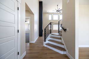 Stairway featuring wood finished floors, ceiling fan with notable chandelier, and baseboards