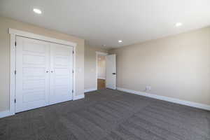Unfurnished bedroom featuring a closet, recessed lighting, baseboards, and dark carpet