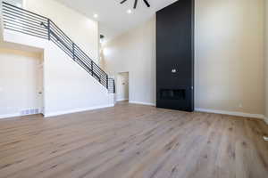 Unfurnished living room featuring ceiling fan, visible vents, a high ceiling, stairs, and light wood finished floors