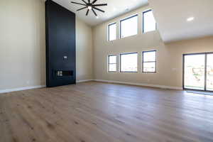 Unfurnished living room with a large fireplace, light wood finished floors, a high ceiling, and a ceiling fan