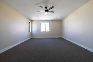 Spare room with dark colored carpet, baseboards, and a ceiling fan