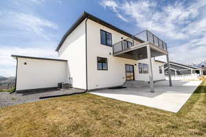 Rear view of house with a yard, a balcony, stucco siding, and a patio area