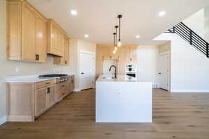 Kitchen with baseboards, a sink, light brown cabinetry, stainless steel appliances, and light wood-style flooring