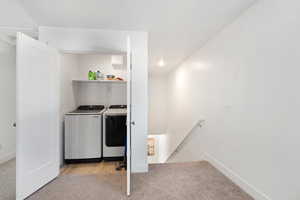 Clothes washing area featuring light colored carpet, separate washer and dryer, laundry area, and baseboards