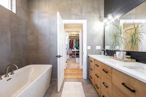 Bathroom featuring a freestanding bath, a sink, tile walls, double vanity, and tile patterned floors