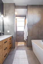 Full bathroom featuring tile patterned flooring, tile walls, a freestanding tub, and vanity