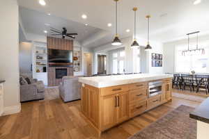 Kitchen featuring a center island, a brick fireplace, a ceiling fan, light wood-style floors, and pendant lighting