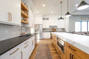 Kitchen featuring open shelves, decorative light fixtures, a sink, appliances with stainless steel finishes, and light wood-style floors