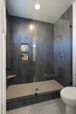 Bathroom with tile patterned floors, a tile shower, and toilet