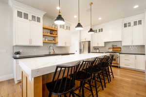 Kitchen featuring tasteful backsplash, open shelves, custom exhaust hood, appliances with stainless steel finishes, and a sink