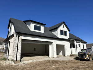 View of side of house with a shingled roof, driveway, and stone siding
