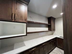 Kitchen with open shelves, dark brown cabinetry, light stone countertops, and recessed lighting