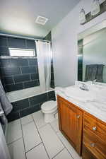 Bathroom featuring tile patterned floors, visible vents, toilet, vanity, and tiled shower / bath combo