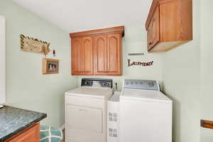 Clothes washing area featuring visible vents, washing machine and dryer, and cabinet space