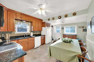 Kitchen featuring ceiling fan, white appliances, dark stone countertops, a sink, and brown cabinets