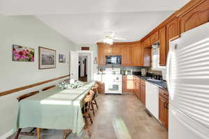 Kitchen with white appliances, dark countertops, brown cabinets, ceiling fan, and a sink