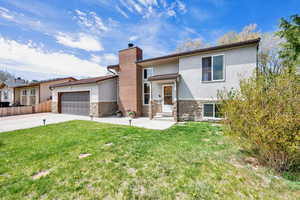 View of front of home featuring stucco siding, a chimney, stone siding, an attached garage, and a front lawn