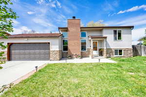 View of front of property featuring a front yard, stone siding, a garage, stucco siding, and driveway
