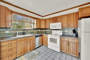 Kitchen with crown molding, light tile patterned floors, white appliances, tasteful backsplash, and a sink
