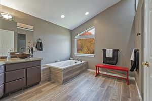 Full bathroom featuring vanity, baseboards, vaulted ceiling, a bath, and wood finished floors