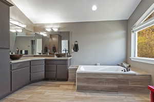 Bathroom with a sink, double vanity, wood finished floors, vaulted ceiling, and a garden tub