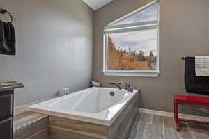 Full bath featuring a bath, baseboards, and wood finished floors