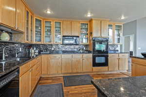 Kitchen featuring glass insert cabinets, wood-style floors, backsplash, black appliances, and a sink