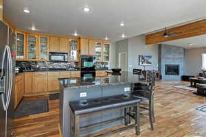 Kitchen featuring a kitchen breakfast bar, a ceiling fan, black appliances, light wood finished floors, and backsplash