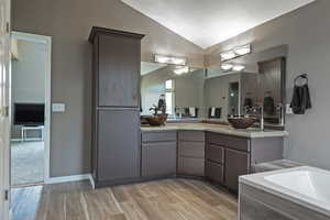 Full bathroom with wood finished floors, double vanity, a sink, and vaulted ceiling