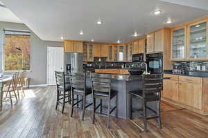 Kitchen with glass insert cabinets, black appliances, recessed lighting, a center island, and decorative backsplash