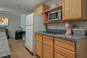 Kitchen with open shelves, black electric cooktop, stainless steel microwave, and light carpet