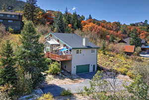 Exterior space with an attached 2-car garage, a view of trees, a wooden deck, and the driveway