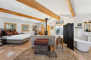 Bedroom with a wood stove, multiple windows, vaulted ceiling with beams, and recessed lighting