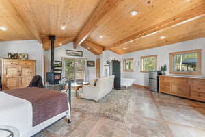 Bedroom with lofted ceiling with beams, a wood stove, multiple windows, wooden ceiling, and freestanding refrigerator