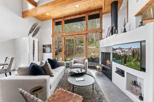 Living room with beamed ceiling, a towering ceiling, a warm lit fireplace, and concrete flooring