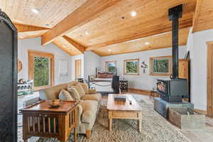 Living area with vaulted ceiling with beams, a wood stove, wooden ceiling, baseboards, and recessed lighting