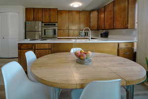 Kitchen with a sink, light countertops, double ovens, freestanding refrigerator, counter stovetop, and brown cabinetry