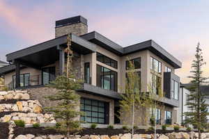 Property exterior at dusk with stucco siding, a chimney, and stone siding