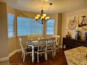 Dining room with a textured ceiling, dark wood-style flooring, a notable chandelier, and baseboards