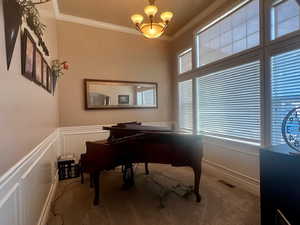 Carpeted home office featuring a notable chandelier, ornamental molding, a wainscoted wall, visible vents, and a decorative wall