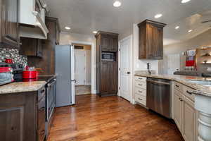 Kitchen featuring appliances with stainless steel finishes, dark brown cabinetry, decorative backsplash, wood finished floors, and light stone counters